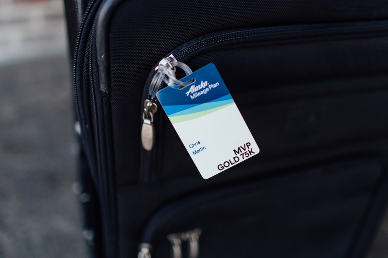 Photo of an Alaska Airlines MVP Gold 75K luggage tag on a black roller bag suitcase.