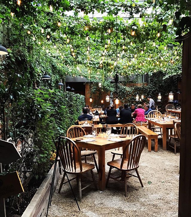 This is a photo of an outdoor restaurant with seating areas under lush greenery.