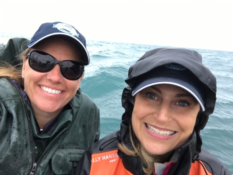 This is a photo of Jodi Harskamp with Jenny Stansel in rain gear out on a boat fishing for salmon in Alaska.