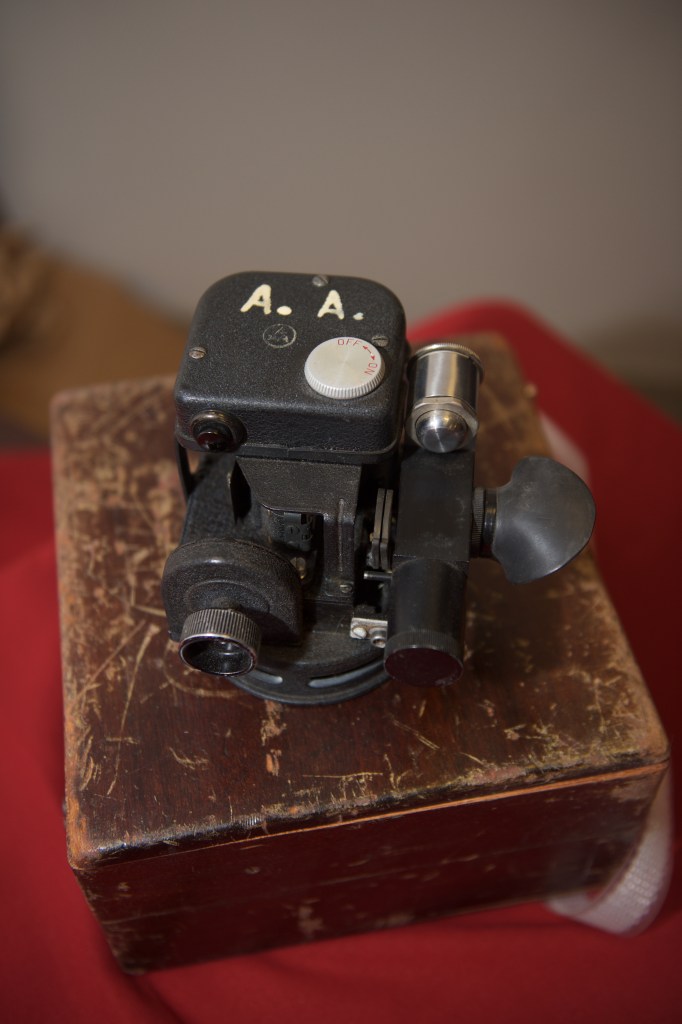 This is a photo of a black sextant sitting on top of a worn wooden box.