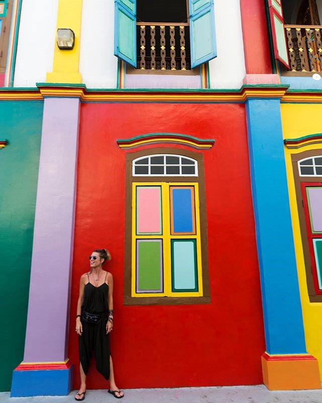 This is a photo of a woman standing in front of a brightly colored rainbow building. Each column, frame is painted a different bright color.